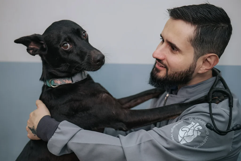 Dr. Guilherme Matteucci sorrindo para um cão preto que apoia as patas em seu ombro