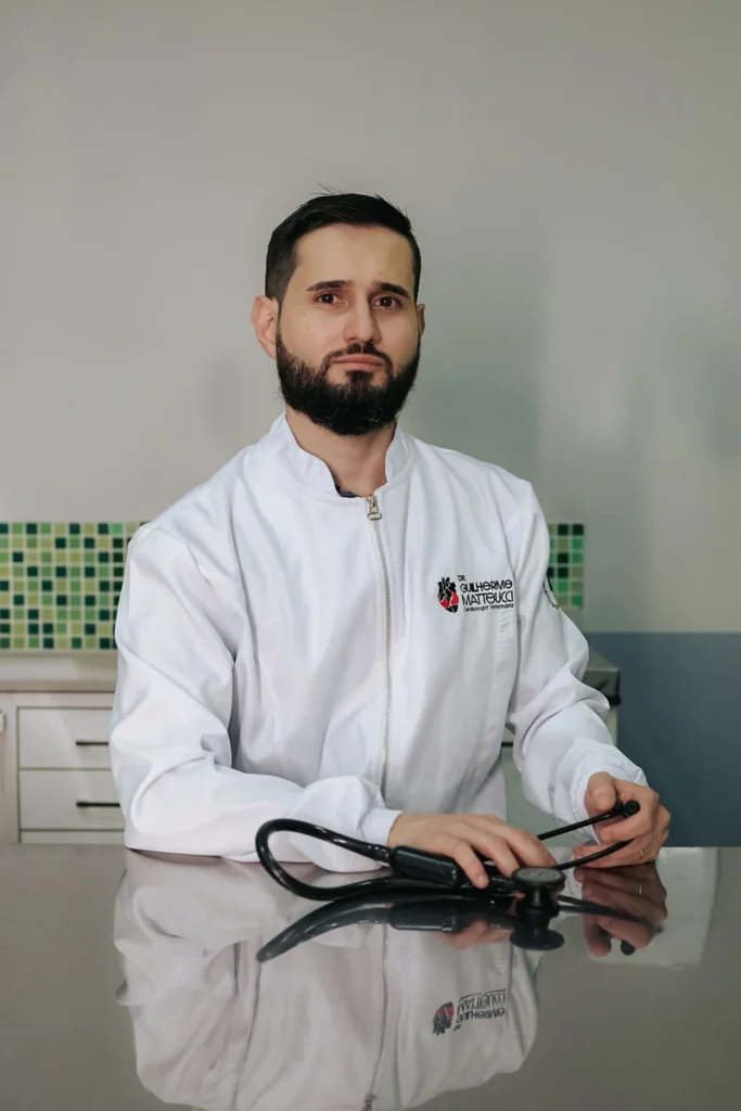 Dr. Guilherme Matteucci de jaleco branco segurando o transdutor do ecocardiograma no consultório