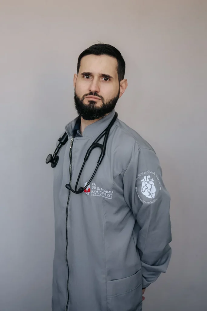 Dr. Guilherme Matteucci de jaleco cinza com a marca e estetoscópio no pescoço